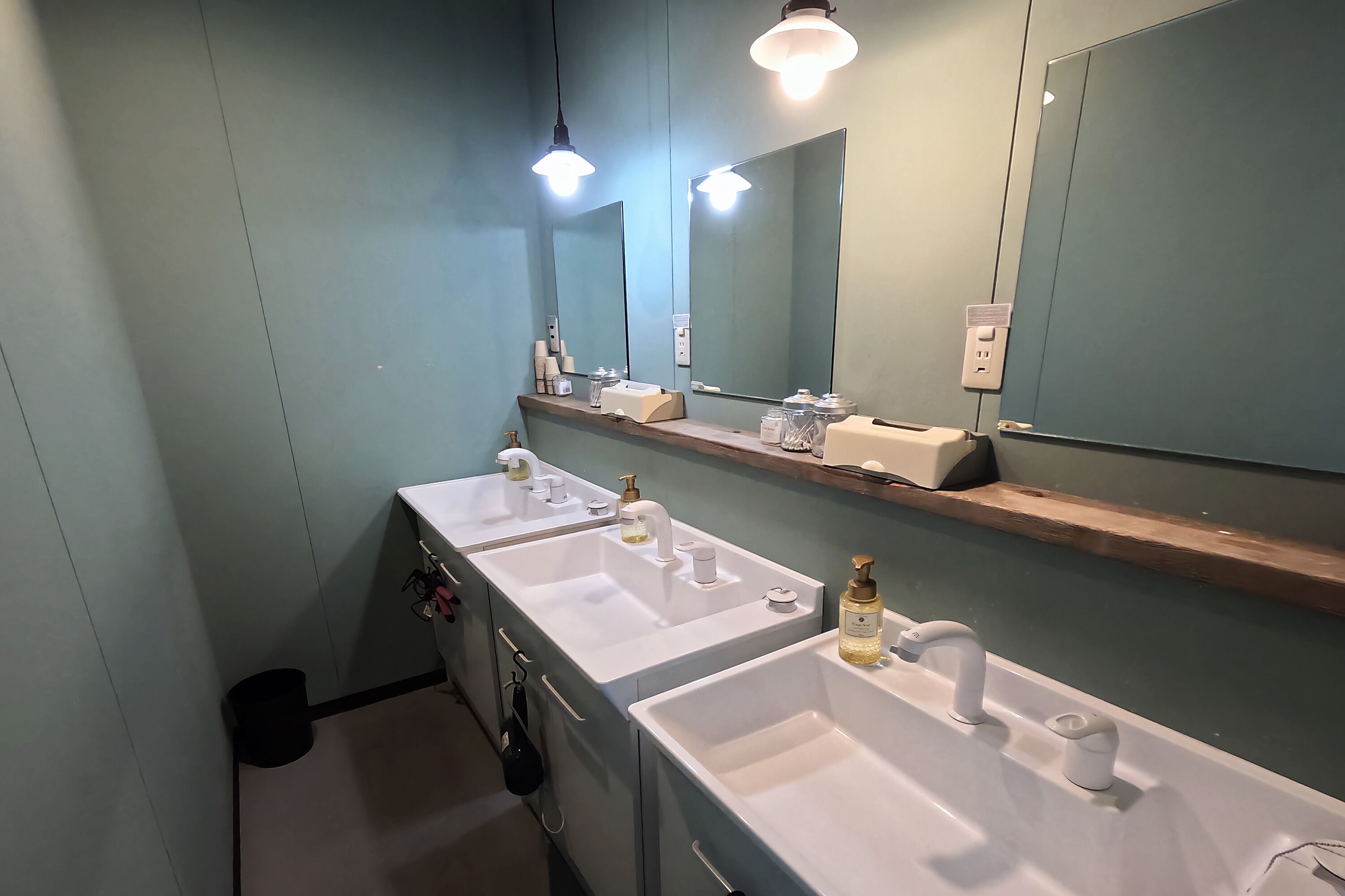 A bathroom with three sinks, a mirror, and overhead lighting.