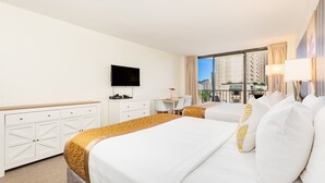 Ein Hotelzimmer mit zwei Betten, einem Fernseher, einem Schreibtisch mit Stuhl und Blick auf die Stadt.