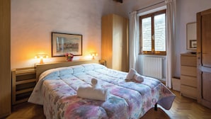 A bedroom with a bed, wooden headboard, a painting, a window with curtains, and a wooden dresser.
