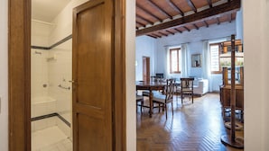 A wooden door leading to a bathroom with a shower and a dining area with a wooden table and chairs.