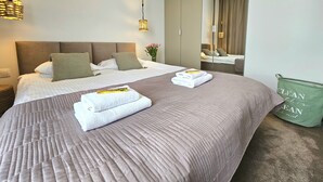 A neatly made bed with folded towels, a bedside table with a basket, and a green bag with the text "CLEAN THINGS CLEAN MIND" on the floor. - Apartament Nefryt - 365PAM (Sarbinowo)