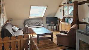 Un soggiorno in stile loft con travi a vista in legno, soffitto spiovente, una grande finestra, un camino e un televisore.