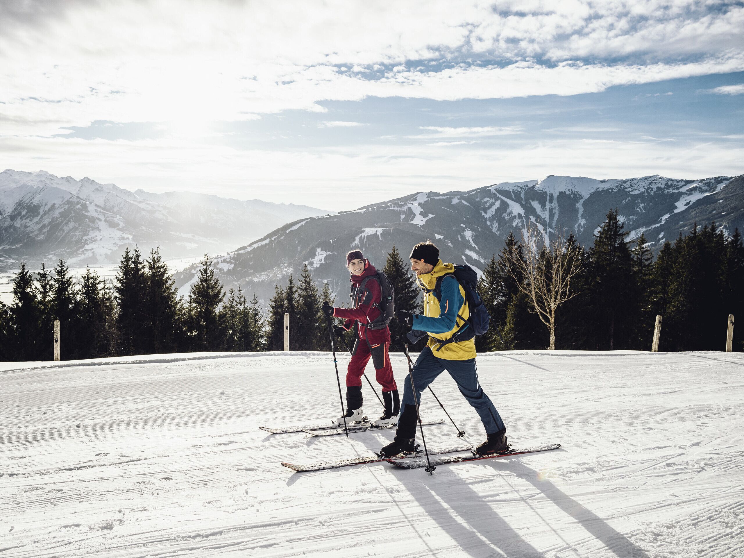 Een besneeuwd landschap met bergen op de achtergrond en twee personen aan het skiën.