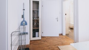 A hallway with a wooden floor, a white door, and a metal rack with cleaning supplies.