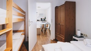 A compact room with bunk beds, a wooden wardrobe, a kitchenette, and a dining area.