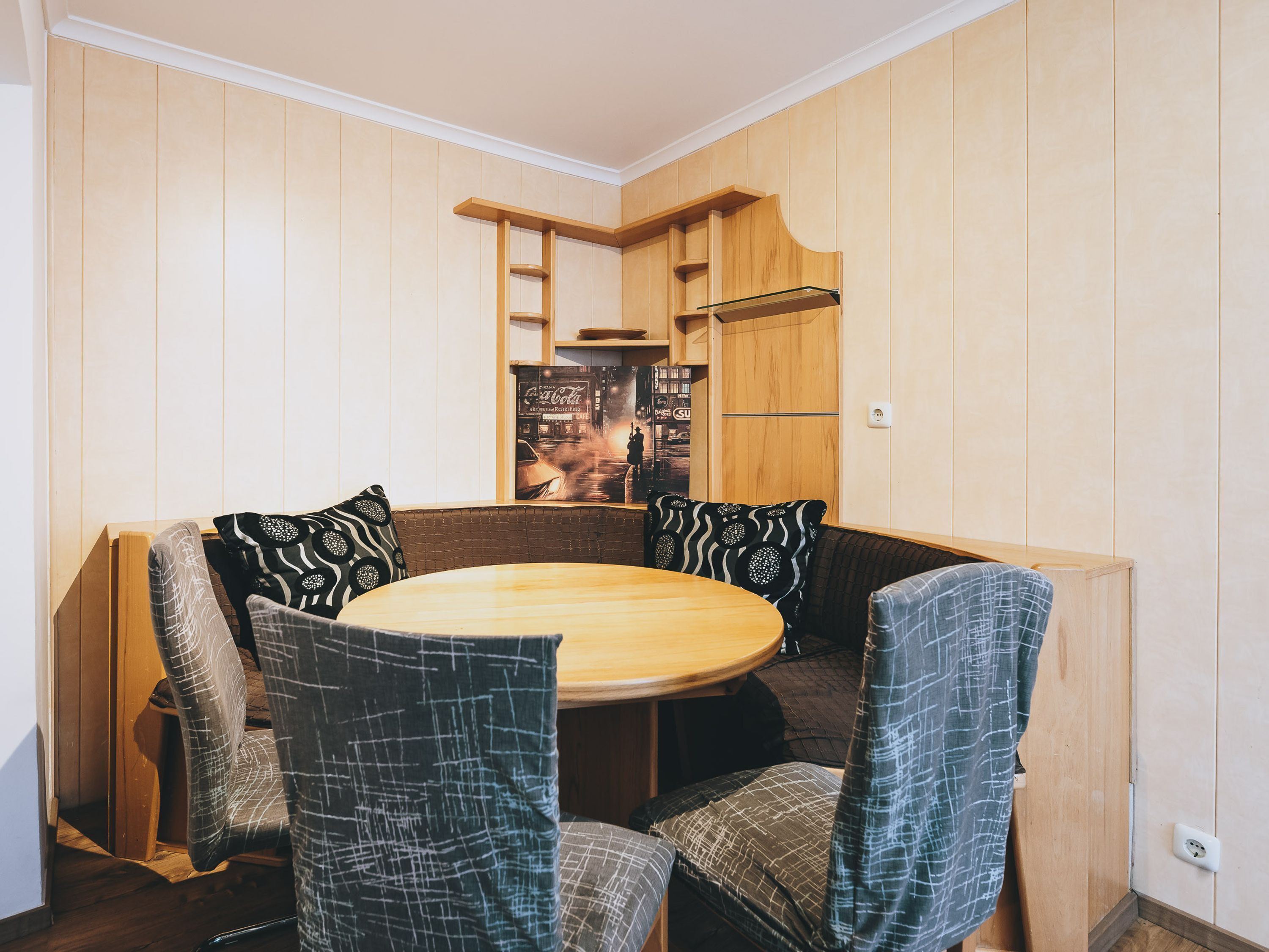 A dining area with a round table and four chairs, wooden panel walls, and a poster on the wall.
