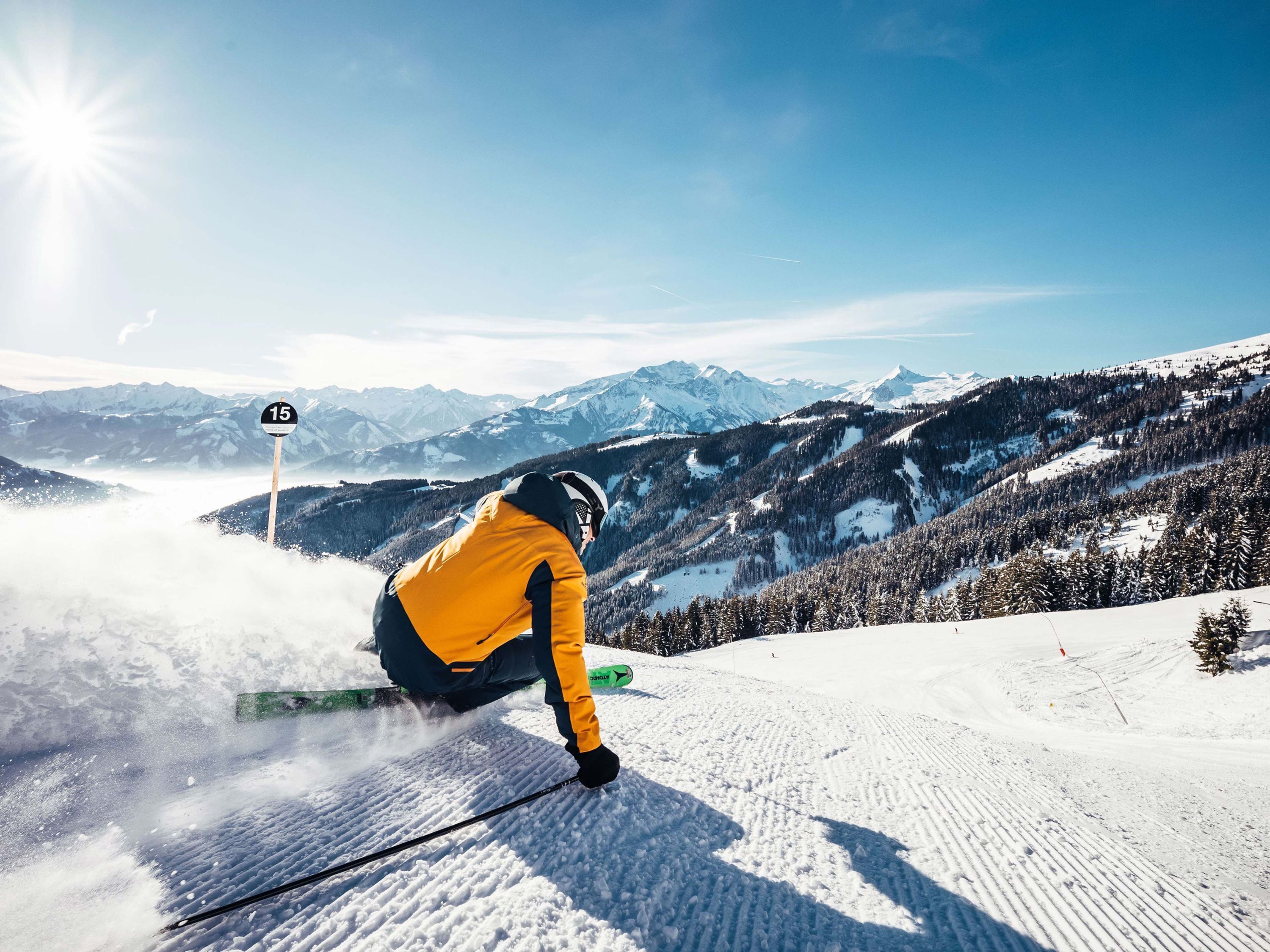 Un skieur sur une pente enneigée, avec un ciel dégagé et des montagnes à l’horizon.
