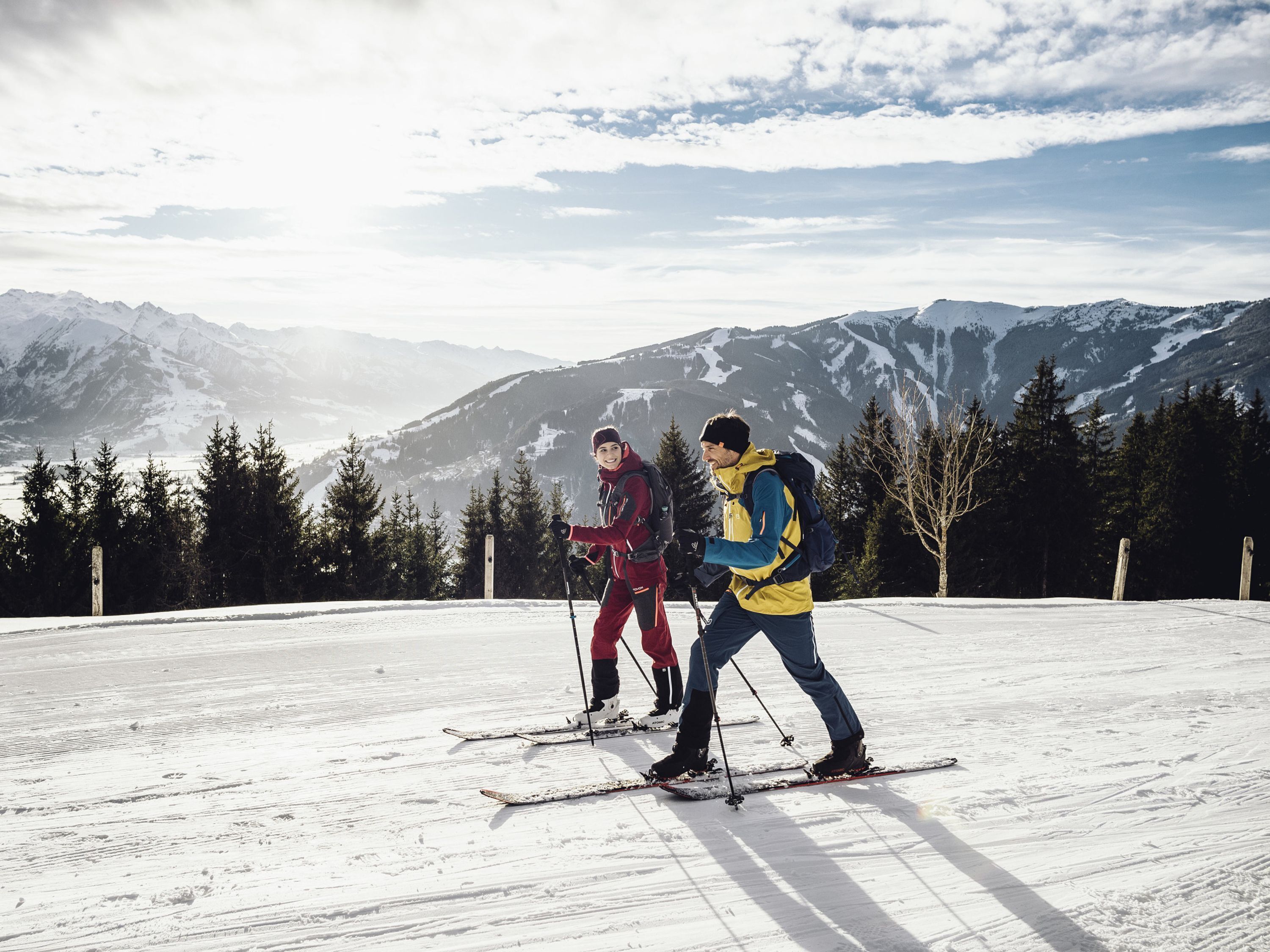 Two people skiing on a snowy slope with mountains in the background.
