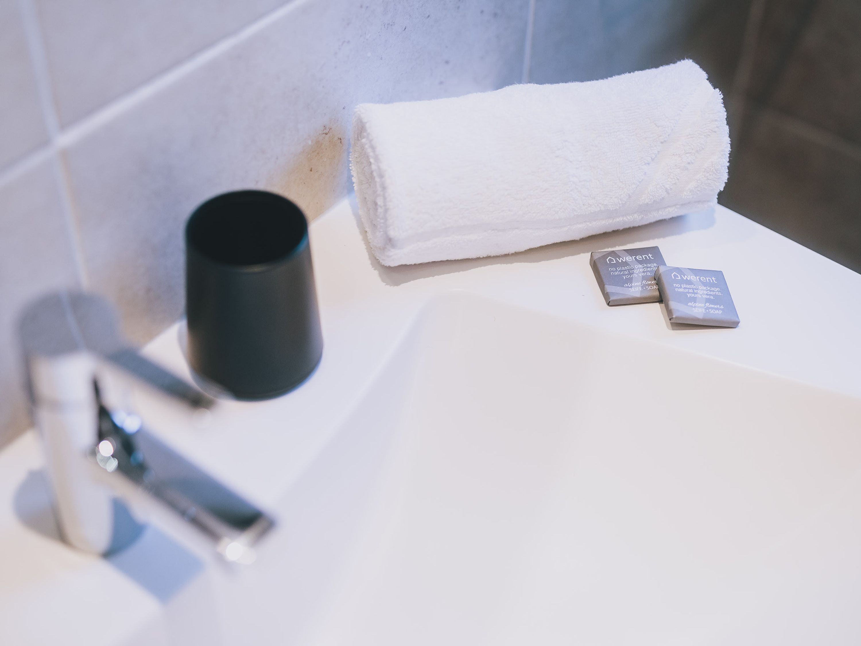 Un lavabo de salle de bain avec une serviette blanche, une tasse noire et deux savons.