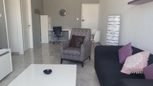 A modern living room with a white coffee table, a patterned armchair, a black sofa with purple cushions, and a large abstract painting on the wall. - Great views apartment. (Limassol)
