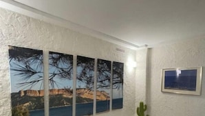 Una habitación con un amplio ventanal que muestra un paisaje costero, un cactus y un cuadro en la pared.