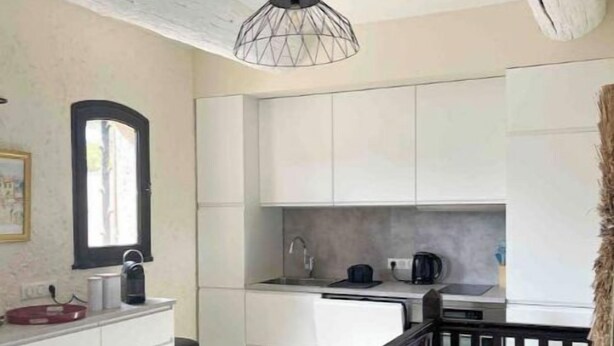 Una cocina moderna con armarios blancos, una lámpara colgante y una escalera de madera.