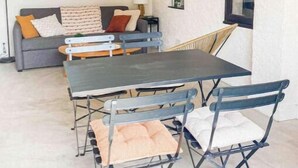 Una sala de estar con un sofá, una mesa de centro y una mesa de comedor con sillas. Hay un televisor montado en la pared y una ventana con vistas.