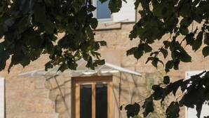 A stone building with a wooden door, a table with a bowl of fruit and a glass, and a chair. - La Maison des Monts d'or (Saint-Germain-au-Mont-d'Or)