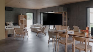 A modern living room with a large flat-screen TV, a sofa, a coffee table, and a dining area with chairs and a laptop. - La Maison des Monts d'or (Saint-Germain-au-Mont-d'Or)