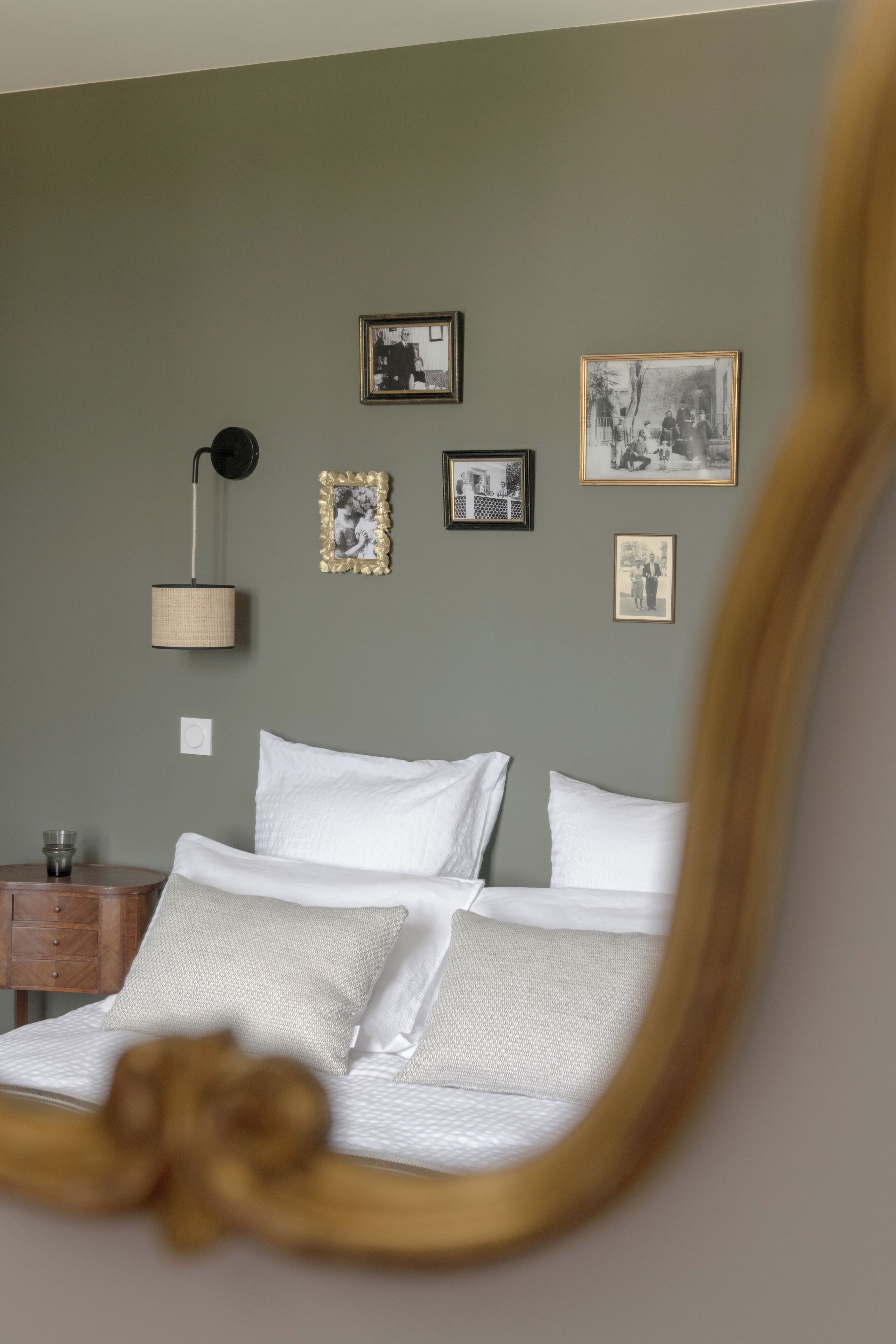 Un dormitorio con cama, mesita de noche, lámpara y cuadros en la pared.