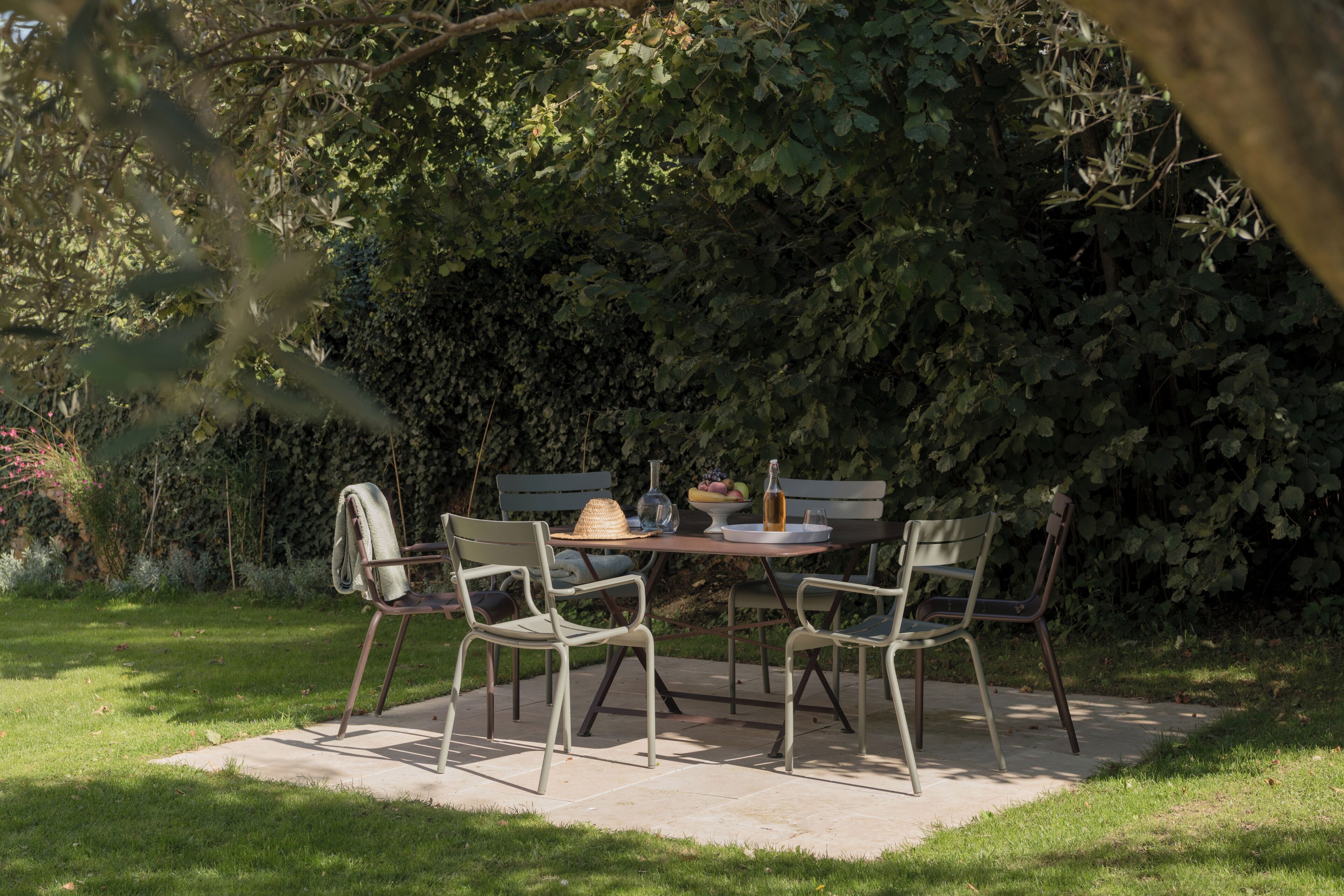 Un patio ajardinado con una mesa y cuatro sillas, rodeado de abundante vegetación.