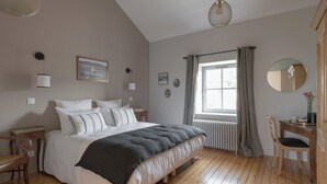 A bedroom with a bed, bedside table, chair, window with curtains, and wall-mounted decor. - La Maison des Monts d'or (Saint-Germain-au-Mont-d'Or)