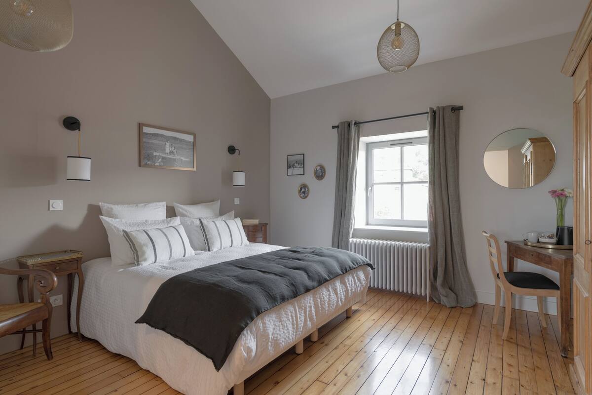 A bedroom with a bed, bedside table, chair, window with curtains, and wall-mounted decor.
