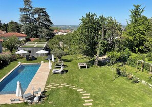 A rectangular swimming pool with lounge chairs and umbrellas, surrounded by well-maintained grass and trees. - La Maison des Monts d'or (Saint-Germain-au-Mont-d'Or)