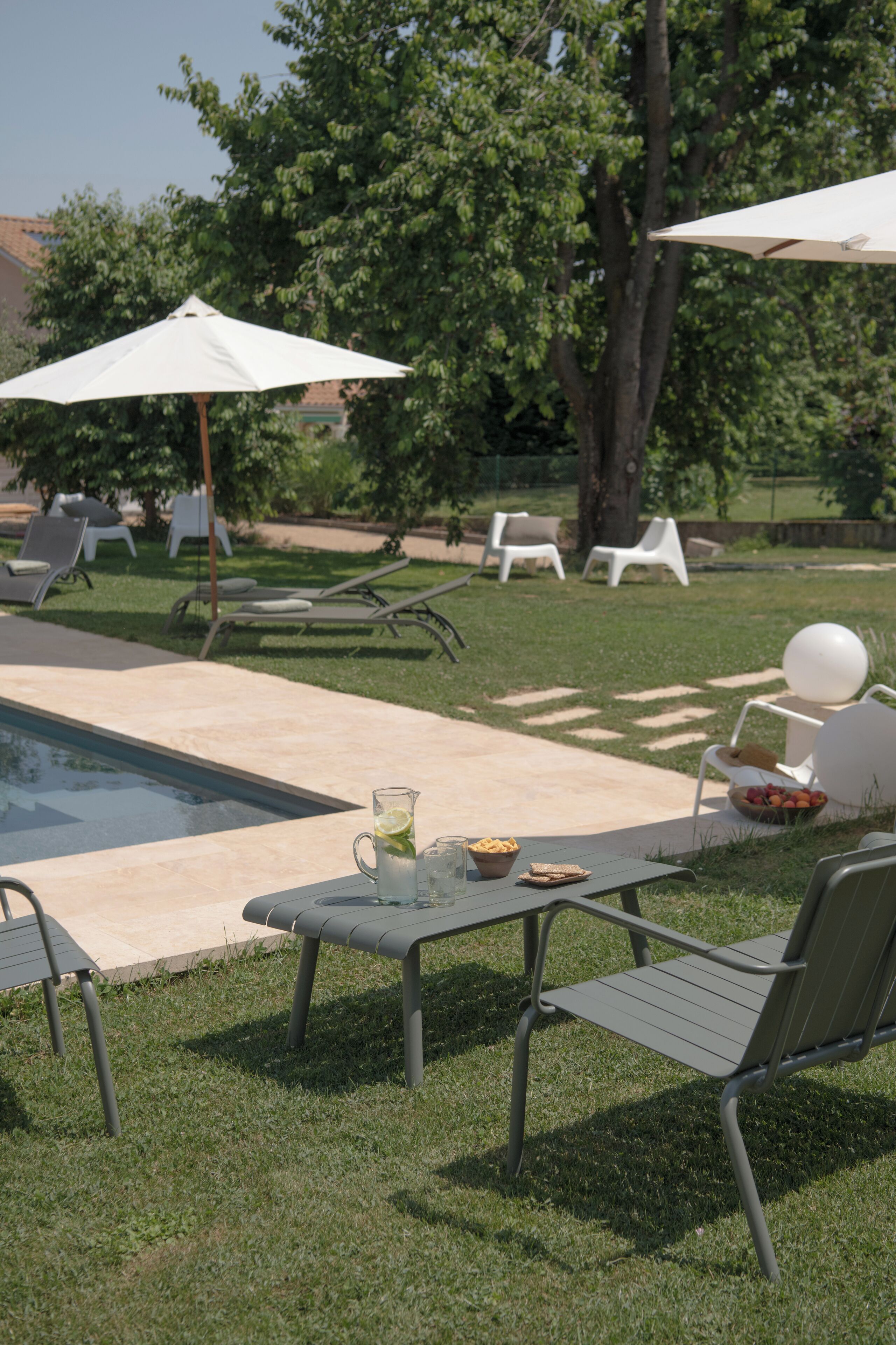Un espace aménagé au bord de la piscine, avec des chaises longues, des parasols et une table sur laquelle sont disposés une carafe et des en-cas.