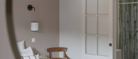 A bedroom with a bed, a chair, a desk, and a door leading to another room.
