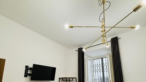 A room with a television mounted on the wall, a standing fan, a window with curtains, and a ceiling light fixture. - Prime Rooms Verdi (Florence)