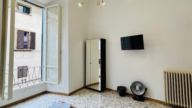A bedroom with a large bed, a ceiling light, a radiator, and a TV on the wall. - Prime Rooms Verdi (Florence)