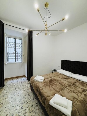 A bedroom with a large bed, a chandelier, a window with curtains, and a door. - Prime Rooms Verdi (Florence)