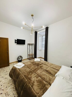 A bedroom with a large bed, a TV mounted on the wall, a fan, and a window with curtains. - Prime Rooms Verdi (Florence)