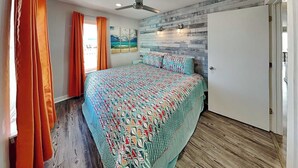 Un dormitorio con una cama, cortinas anaranjadas, un ventilador de techo, una lámpara de pared y una puerta.