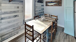 Un comedor con una mesa y sillas de madera, un ventanal con vistas y una pared decorada con un cuadro de un tiburón.