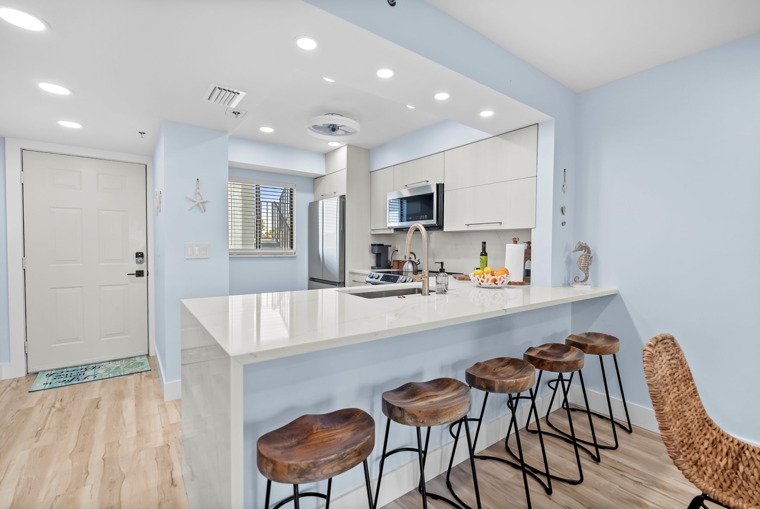 Una cocina moderna con una isla blanca, taburetes de bar y una silla de mimbre.