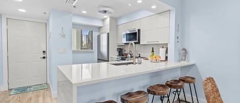 Una cocina moderna con una isla blanca, taburetes de bar y una silla de mimbre.