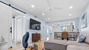 A modern living room with a sectional sofa, a wooden coffee table, and a flat-screen TV mounted on the wall. - Admirals Bay 152 | Canal Front Condo, Balcony + Community Pool (Fort Myers Beach)