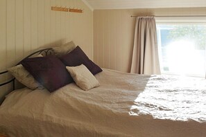 Ein Bett mit einem gemusterten Überwurf, einem Kopfteil und einem Fenster mit Vorhängen.