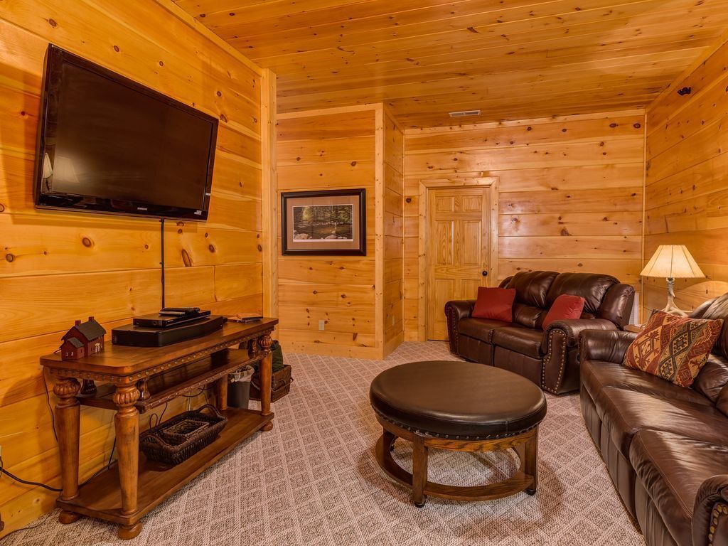 A log cabin interior with a wooden TV stand, leather sofa, and a framed picture on the wall.