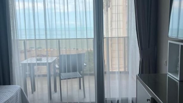 Ein Zimmer mit Bett, Schreibtisch und Meerblick durch durchsichtige Vorhänge.