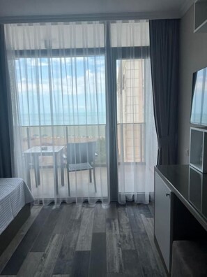 Ein Zimmer mit Bett, Schreibtisch und Meerblick durch durchsichtige Vorhänge.