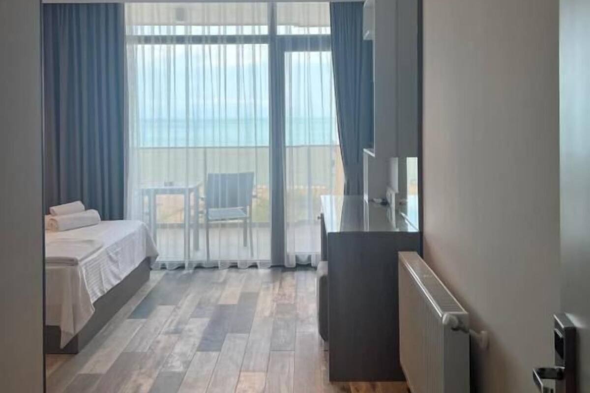 A hotel room with a bed, a desk, a chair, and a large window with curtains.