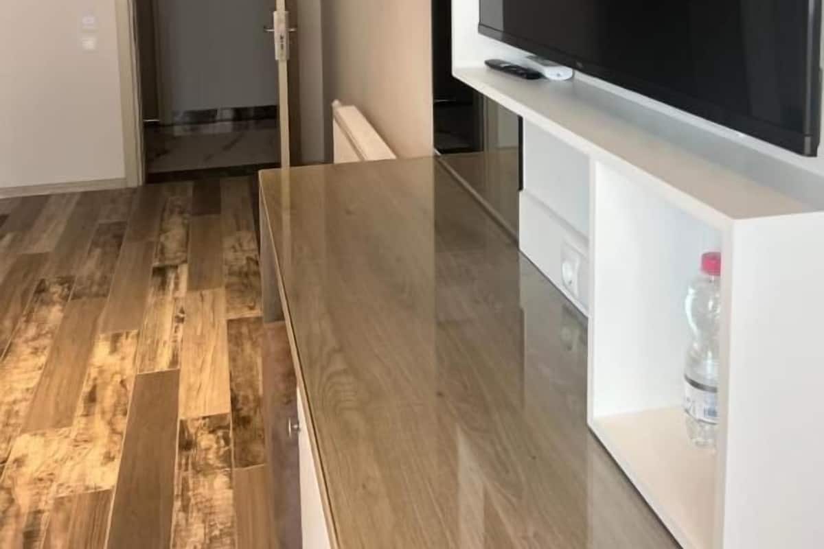 A modern living room with a large flat-screen TV mounted on a white cabinet, hardwood flooring, and a door leading to another room.