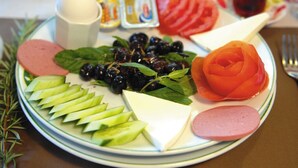 Ein Teller mit Gurkenscheiben, Käse, Oliven, einer tomatenförmigen Rose und Fleisch.