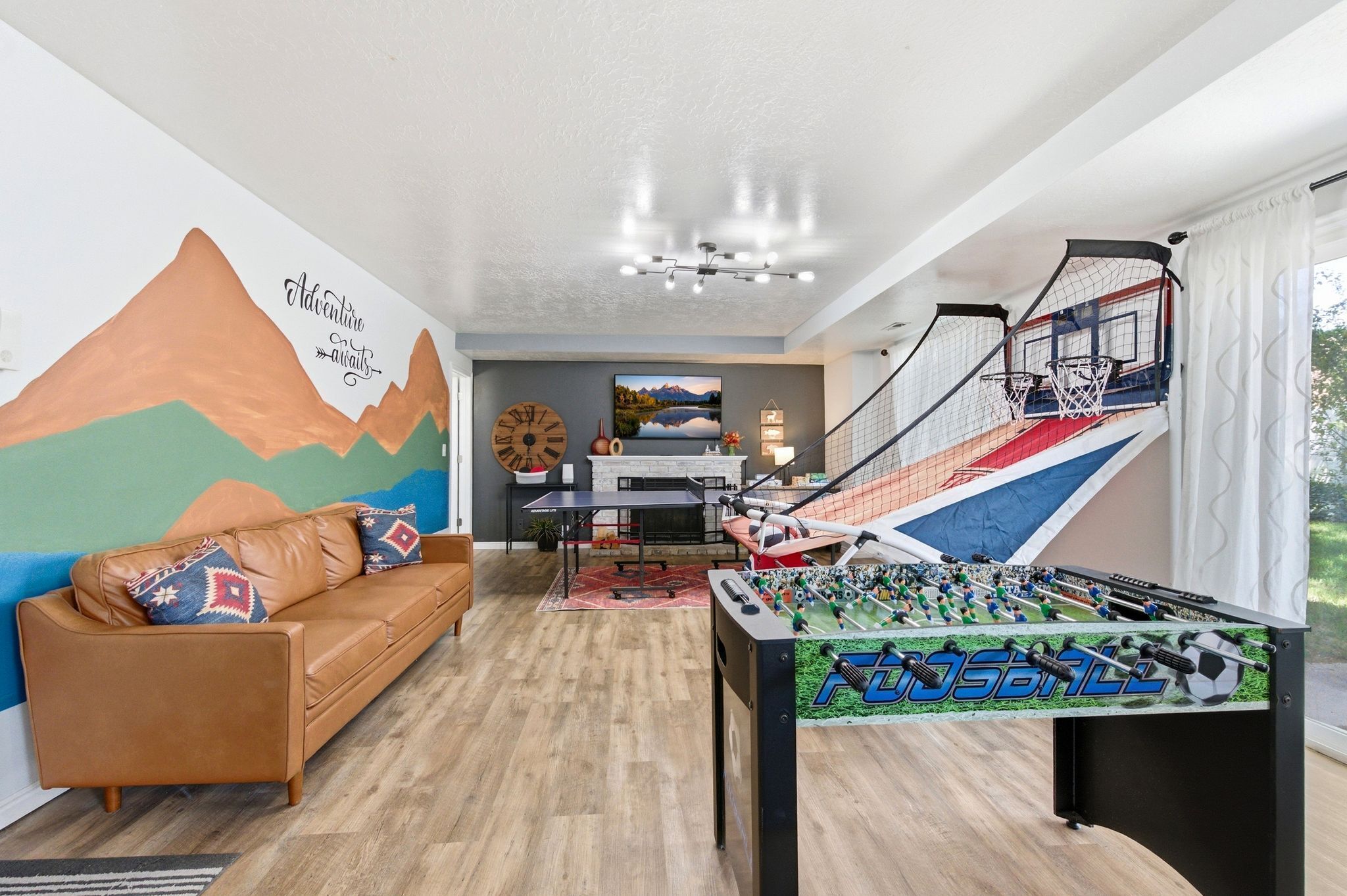 A living room with a foosball table, a sofa, a wall mural, and a staircase.