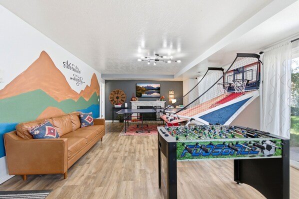 Un salon avec une table de baby-foot, un canapé, une fresque murale et un escalier.