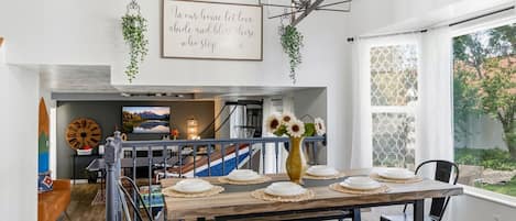 A dining area with a wooden table set for four, a vase with flowers, and a staircase leading to a living area.