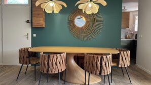 A dining area with a large wooden table surrounded by six chairs with a unique woven design. There are two pendant lights with a floral pattern hanging above the table. A circular wall art piece with a sunburst design is visible on the wall. - Magnificent air-conditioned duplex, 3 bedrooms, 2 large terraces, swimming pool & beach on foot! (Le Lavandou)