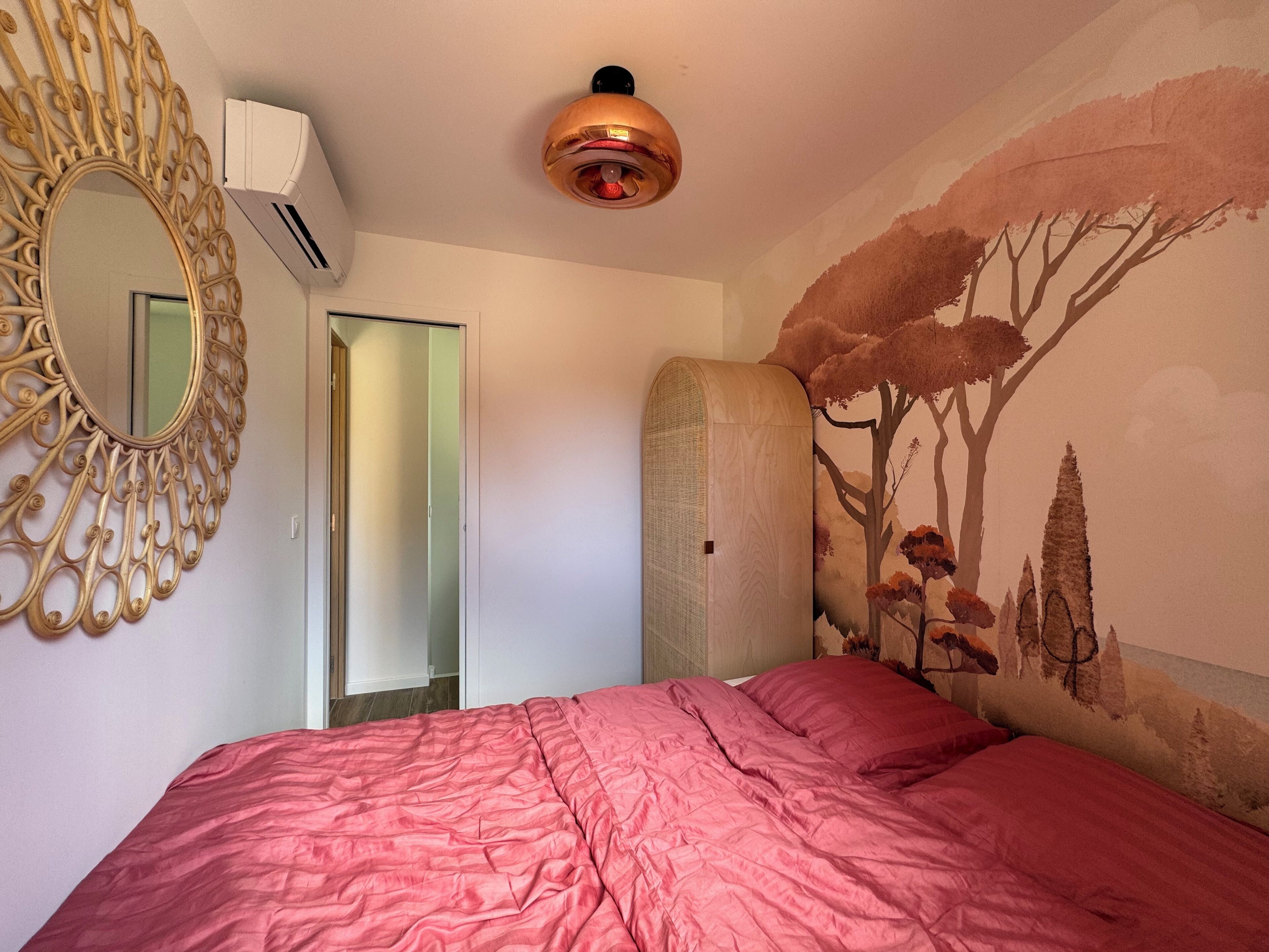 Een slaapkamer met een bed, een grote spiegel, een plafondlamp en een muurschildering.