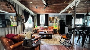 A spacious living room with a leather sofa, a coffee table, and a dining area with a table and chairs. - The Duck Blind at Cooter Creek Cabins (Elberton)