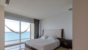 A bedroom with a large bed, a nightstand, and a view of the sea through a large window. -  H2 Bocagrande Vista al Mar-Bahía (Cartagena)