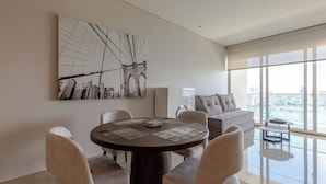 A modern living room with a round dining table, beige chairs, a large abstract painting, a sofa, and a view of the city through large windows. -  H2 Bocagrande Vista al Mar-Bahía (Cartagena)